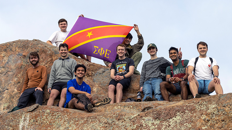 Outdoor photo of fraternity members holding the SigEp flag